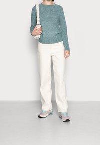 Pull en tricot couleur sarcelle, pantalon blanc à jambes larges et baskets multicolores. Le pull possède un col rond et une texture côtelée ; les baskets présentent des détails translucides.