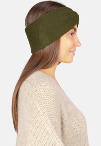 Bandeau vert en tricot avec un design torsadé, présentant une texture douce et une large bande ; accessoire porté avec un pull beige clair.