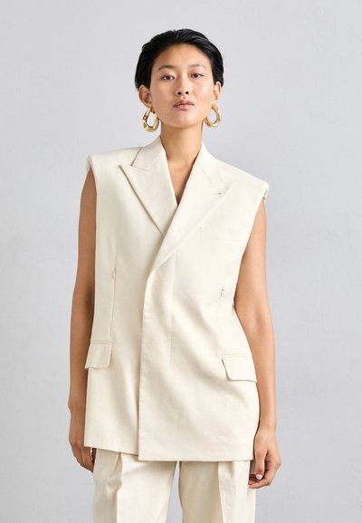 Blazer sin mangas color marfil hecho de tejido estructurado, que presenta un diseño de doble botonadura, dos bolsillos frontales y detalles de costura sutiles.