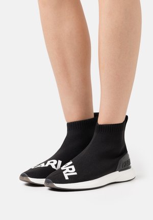 Schwarze gestrickte Sneaker im Sockendesign mit einem gerippten Kragen, weißen Logodetails auf der Vorderseite und einer kontrastierenden weißen Sohle mit einer strukturierten Ferse.