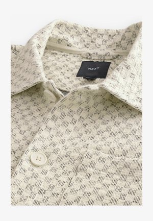 Svetlo béžová košeľa s textúrovým vzorom v čiernych líniách. Obsahuje golier, predné zapínanie na gombíky a štítok s označením "NEXT."