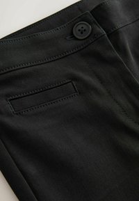 Tissu noir avec une ceinture boutonnée et une poche fendue horizontale avec des coutures nettes le long des bords.