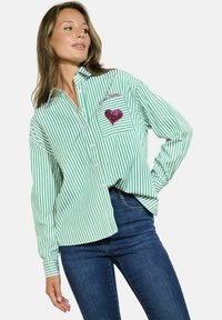 Groen en wit gestreepte button-up shirt met een zak met een roze sequined hart. Lange mouwen met knoopmanchetten, relaxte pasvorm.