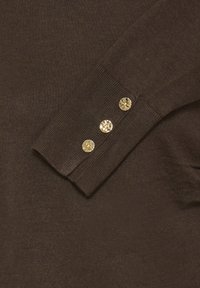 Pruun kootud sviiter soonikkoes mansettidega, millel mansetil on kolm kuldset nööpi. Tekstuur näib pehme ja siidine.