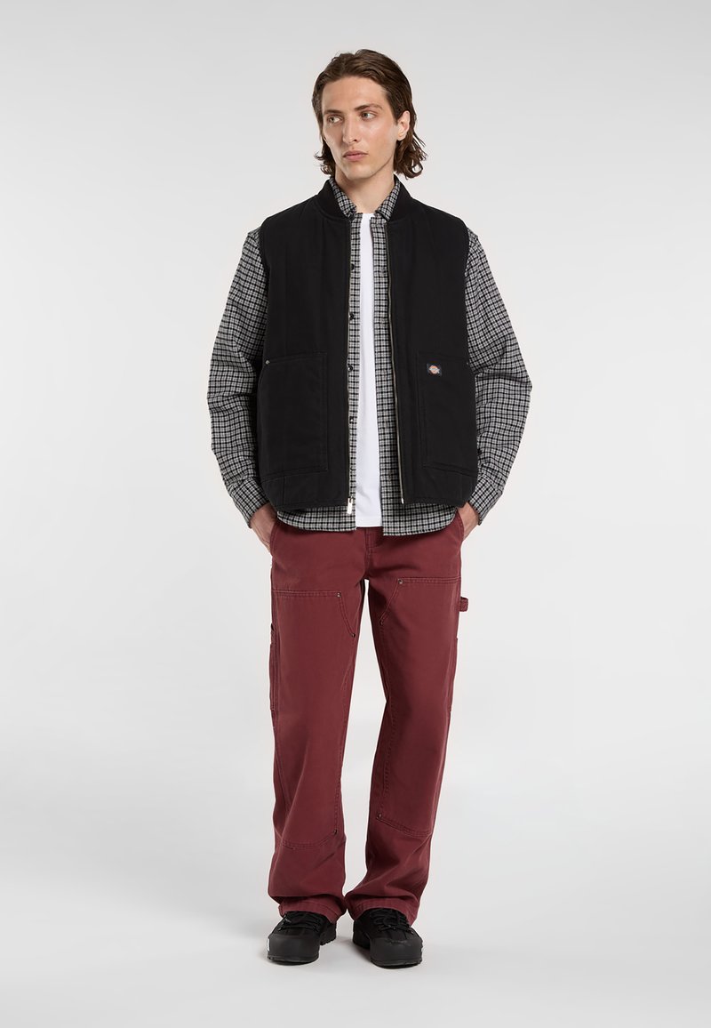 Sort lynlås vest over en ternet skjorte, parret med bordeauxbukser. Vestet har to frontlommer og et logo mærke. Tekstureret stof.