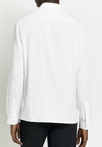 Camicia bianca a maniche lunghe con colletto, texture del tessuto liscia, polsini con bottoni e taglio dritto all'orlo, vista da dietro.