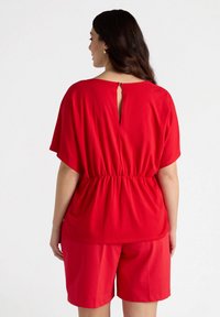 Red short-sleeve top with an elastic waist and keyhole back detail, paired with matching red shorts. Smooth fabric and relaxed design.