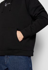 Sudadera con capucha negra hecha de una mezcla de algodón, con un bolsillo frontal, puños acanalados y un logotipo minimalista blanco en el pecho.