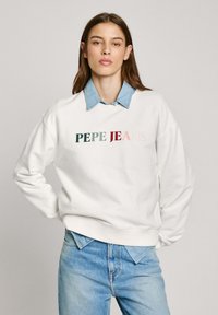 Sudadera blanca con "PEPE JEANS" bordado en verde, rojo oscuro y rosa claro. Usada sobre una camisa de collar azul claro. Ajuste casual.
