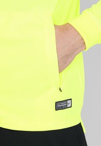 Neon yellow long-sleeve shirt with a zip pocket and black accents. Features a tag reading "AUTHENTIC FOOTBALL" near the hem.