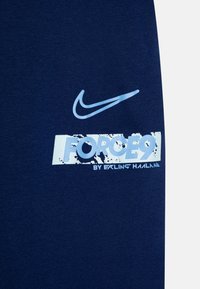 Jūras zila džemperis ar mīkstu tekstūru. Ar gaiši zilu Nike logo un grafiku ar uzrakstu "FORCE9" uz balta nodiluša fona.
