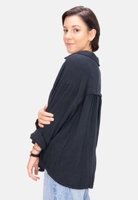 Dunkel strukturiertes Hemd mit aufgerollten Ärmeln, entspannter Passform und abgerundetem Saum, kombiniert mit hellblauen Denim-Jeans.