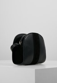 Borsa a tracolla in pelle nera e suede con una forma strutturata, chiusura con cerniera e manico superiore, caratterizzata da una finitura liscia e una texture sottile.