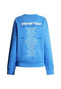 Μπλε φούτερ με την επιγραφή «World Tour Red Bull Racing» και λίστα τοποθεσιών αγώνων του 2026 στην πλάτη, που περιλαμβάνει πόλεις από την Αυστραλία μέχρι το Άμπου Ντάμπι.