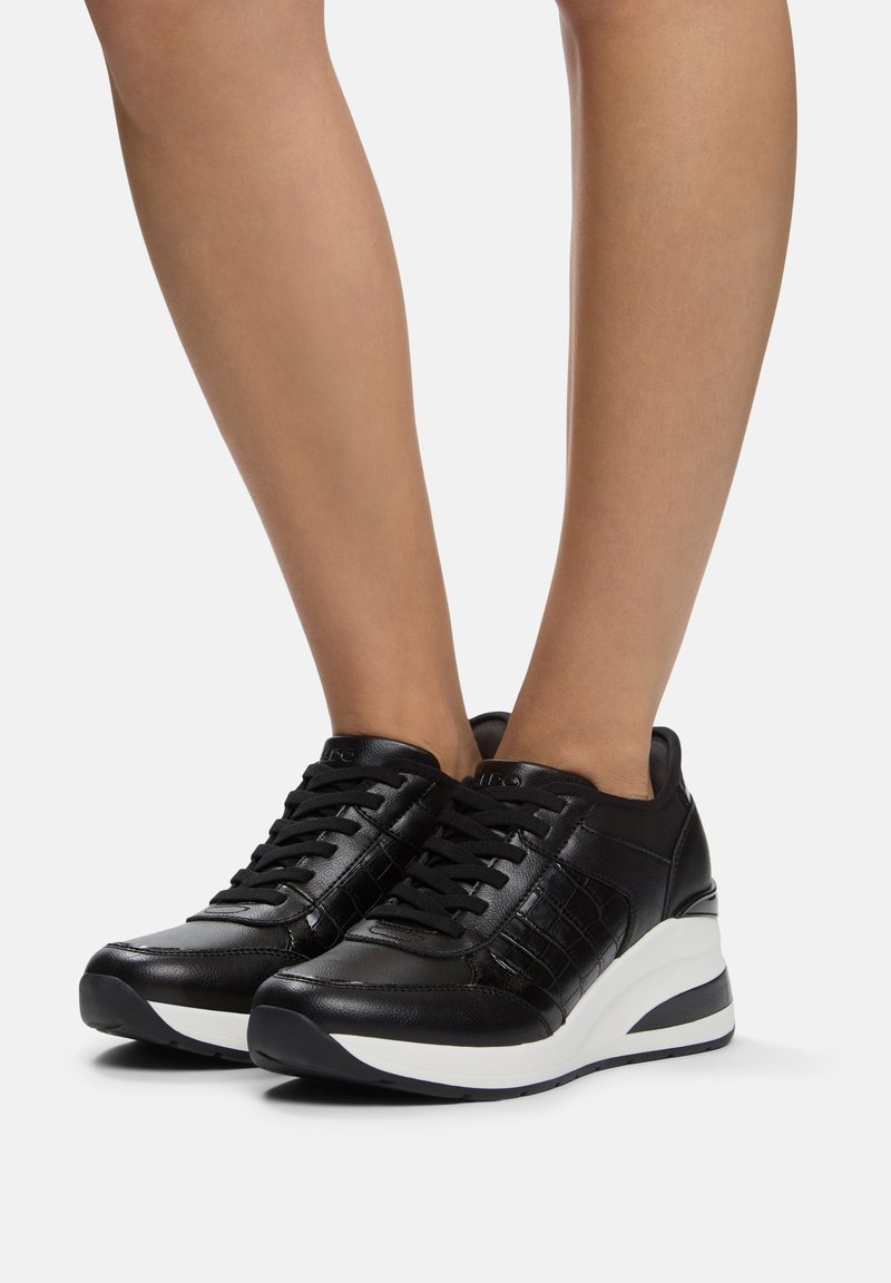 Svarta lädersneakers med ett texturerat mönster, som har en vit mellansula, svart yttersula och snörningsdesign.