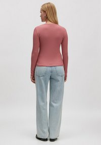 Rippoptik Langarmshirt in Blushrosa, kombiniert mit hellblauen weitgeschnittenen Jeans. Das Oberteil hat eine taillierte Passform und einen Rundhalsausschnitt.