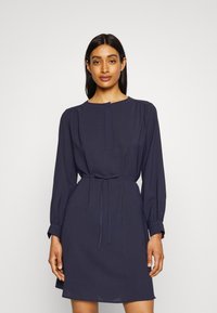 Vestido azul-marinho de manga longa com decote redondo, punhos elásticos, cintura cingida e comprimento até ao joelho, com uma textura suave.