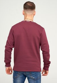 Felpa bordeaux con scollo e polsini a coste, maniche lunghe e orlo dritto, abbinata a jeans in denim chiaro.