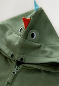 Grøn hoodie med lynlås, med en hætte med blå og orange detaljer og broderede øjne. Blødt stof med et enkelt design.