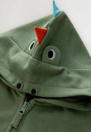 Zelená mikina s kapucí na zip, která má kapuci s modrým a oranžovým akcentem a vyšitými očima. Měkká látka s jednoduchým designem.