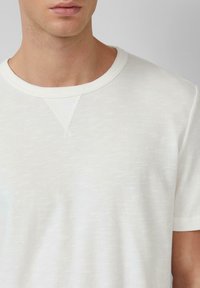 Weißes T-Shirt mit Rundhalsausschnitt aus strukturierter Baumwolle, mit kurzen Ärmeln und feinen Slub-Details. Minimalistisches Design ohne Muster.