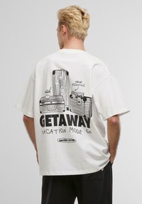 White cotton t-shirt featuring a black graphic print of luggage and the text "GETAWAY VACATION MODE ON" in a casual font.