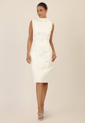 White sleeveless dress with floral textured pattern, fitted shape, and draped neckline. Paired with white strappy sandals.