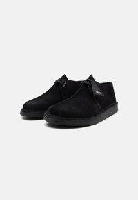 Black suede shoes with a low-cut design, featuring a textured rubber sole, subtle stitching, and a small brand tag on the side.