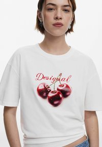 White oversized T-shirt featuring a vibrant graphic of three red cherries with green stems, accompanied by the "Desigual" logo.