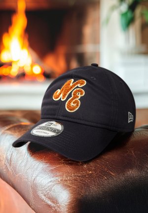 Casquette noire réglable ornée d'un logo brodé texturé "NE" en orange et crème, présentée sur une surface en cuir marron.