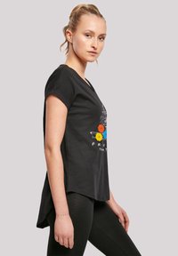 Black t-shirt with short sleeves, featuring a colorful graphic design of a couch and umbrellas. Hemline is slightly longer at the back.
