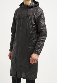 Imperméable noir léger avec capuche, fermeture éclair, deux poches avant et cordons de serrage. Texture semi-brillante et lisse ; longueur jusqu'aux genoux.