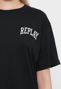 Černé bavlněné tričko s krátkými rukávy a kulatým výstřihem. Na levém prsu se nachází logo "REPLAY" v bílém klenutém písmu. Hladká textura.