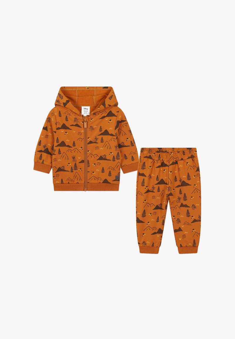 Un sweat à capuche orange zippé et un pantalon assorti présentant des motifs inspirés de la nature avec des montagnes, des arbres et des animaux, accentués de marron foncé et de jaune.