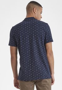 Polo de manga corta azul marino con un patrón geométrico blanco repetido. Fabricado en un tejido suave con cuello clásico y corte relajado.