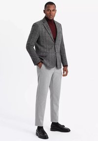 Blazer a quadri grigi con rever appuntito, abbinato a pantaloni grigi chiari e scarpe eleganti nere. Il tessuto ha una finitura texture.
