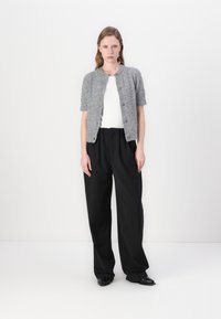 Grå kortermet cardigan med knapper, brukt over en hvit ribbet topp og svarte vide bukser. Glatt tekstur, minimalistisk design.