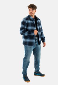 Blauw en zwart geruite flanellen overhemden met knopen, gedragen over een zwart shirt, gecombineerd met lichtblauwe jeans en donkere sneakers met blauwe accenten.