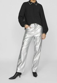 Black long-sleeve shirt with a textured fabric and collared neckline, paired with shiny silver wide-leg pants and pointed black ankle boots.