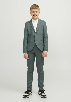 Schiefergrüner Anzug mit einem Ein-Knopf-Jacket, slim-fit Hosen und einem weißen Hemd mit Kragen, kombiniert mit schwarz-weißen Sneakers.