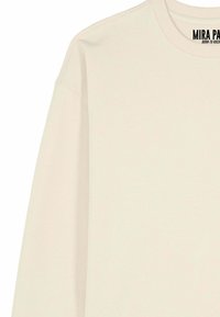 Maglia beige a maniche lunghe con collo rotondo, con la scritta "MIRA PARK Born to Rock" stampata all'interno del colletto sul retro.