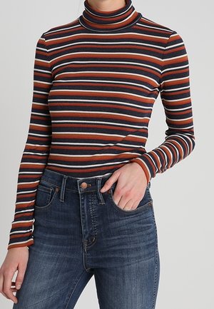 Maglione a collo alto a righe con strette righe orizzontali nei colori blu navy, ruggine e crema, realizzato in un tessuto a costine. Abbinato a jeans blu.