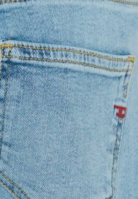Jeans in denim azzurro chiaro con tasca posteriore caratterizzata da cuciture gialle e piccolo dettaglio logo rosso. Il tessuto presenta una classica trama a spina di pesce.