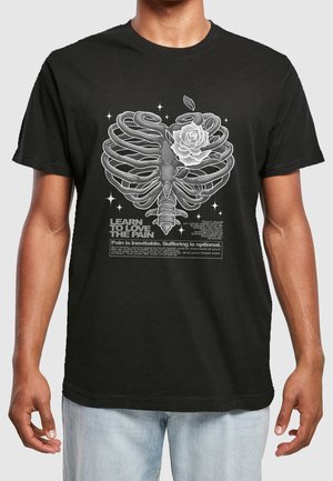 Czarny T-shirt z grafiką białej klatki piersiowej i róży, otoczonej gwiazdami, z motywującym tekstem o bólu i cierpieniu.