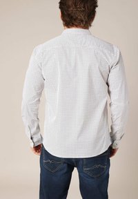 Witte lange mouw shirt met een klein zwart geometrisch patroon, knoopsluiting kraag en manchetten, met een gebogen zoom. Gecombineerd met donkerblauwe jeans.