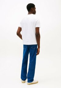 T-shirt bianca in cotone e jeans in denim blu, caratterizzati da una gamba dritta, un tessuto testurizzato e un classico design a 5 tasche. Sneakers bianche completano l'outfit.