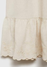 Abito in lino beige con orlo arricciato, bordo a forma di scallop e ricami floreali in tonalità sobria, che mette in evidenza la texture e l'artigianato.