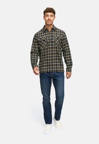 Plaid flannel skjorte i mørkeblå og guld, med to brystlommer, knaplukning foran og lange ærmer, parret med blå jeans og hvide sneakers.