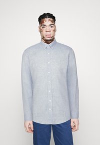 Cămașă button-up de culoare bleu deschis, realizată din in, cu guler clasic, mâneci lungi și un tiv ușor curbat.