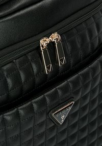 Zwarte, gewatteerde rugzak met goudkleurige dubbele ritsen en een driehoekig logo-accent. Getextureerd oppervlak met een gladde afwerking.